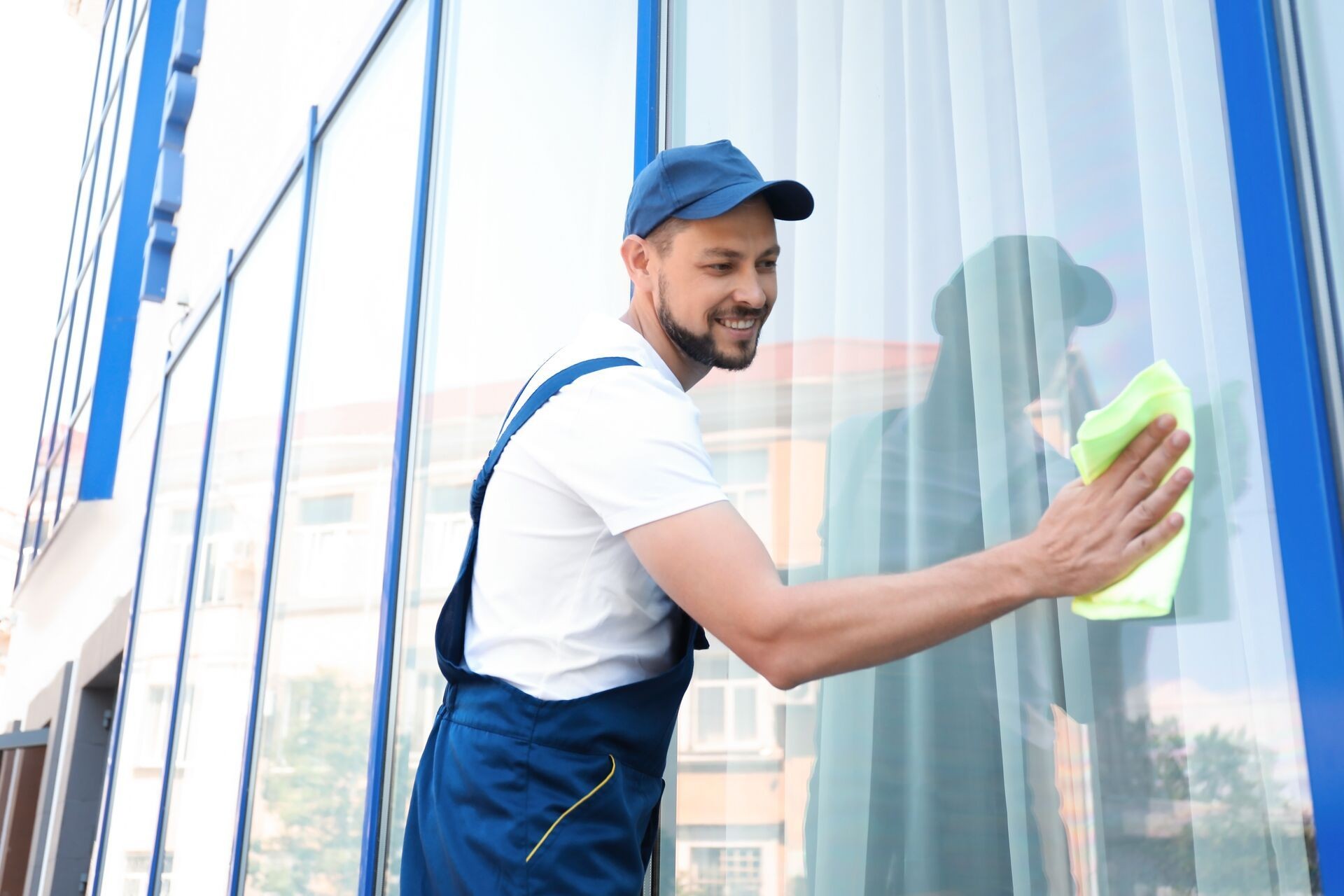 Man in blue uniform cleaning a large glass window with a cloth.