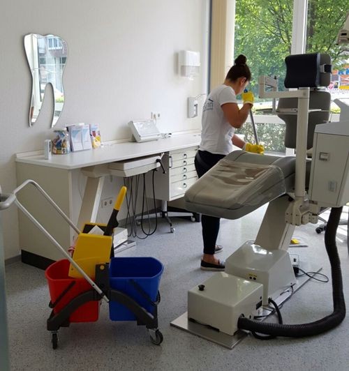 Person cleaning a dental office with cleaning supplies and equipment nearby.